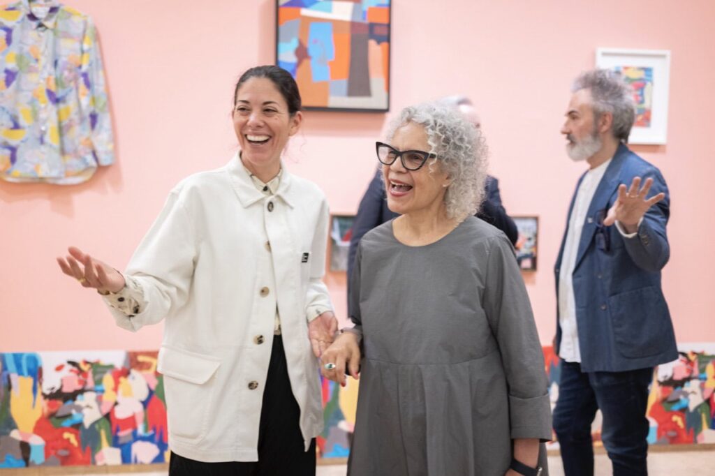 Two women laughing and holding hands in an art gallery.