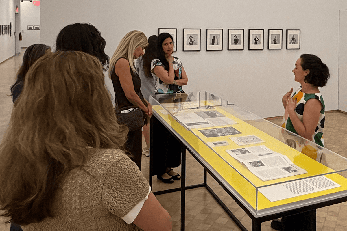 Una guía habla con un grupo de visitantes reunidos alrededor de una vitrina de cristal en una galería de arte.