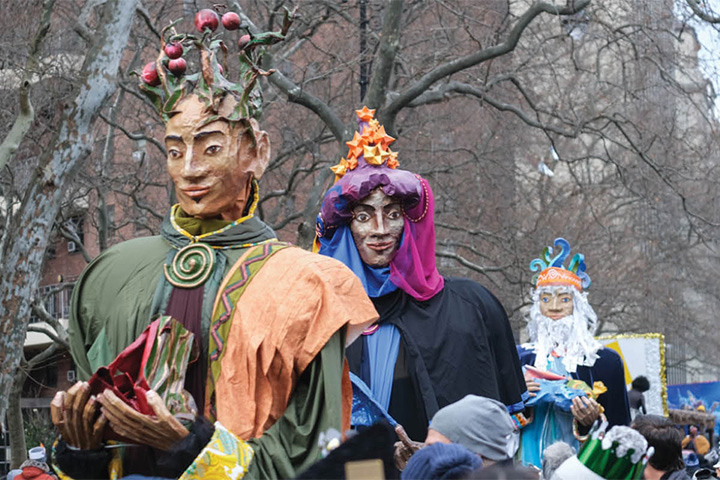 Three giant puppet figures representing the Three Wise Men tower over a crowded city street during a festive parade.