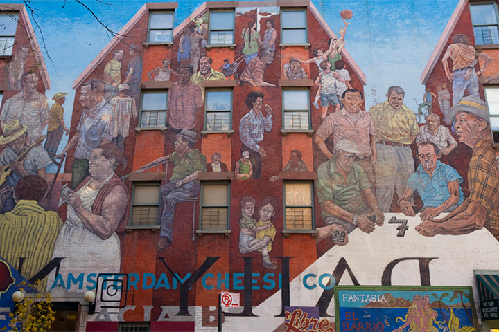A large mural painted across the exterior of a building depicts various community members engaging in daily life.